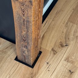 Wegner construction - Rustykalna drewniana kolumna z czarną podstawą, harmonijnie wkomponowana w jasną drewnianą podłogę, tworzy unikalny element wystroju wnętrza.