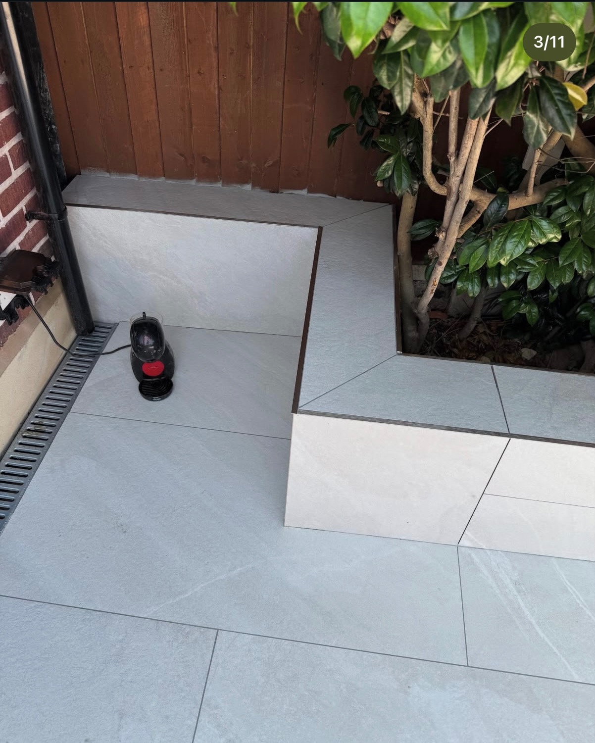 Jasne płytki na zewnątrz tworzą nowoczesną przestrzeń z podwyższonym kwietnikiem i odpływem liniowym. Minimalistyczny design, estetyczne wykończenie.