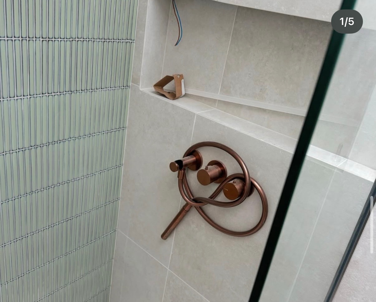 Nowoczesna łazienka z  płytkami typu 'slim' w odcieniach zieleni i miedzianą armaturą. Widoczna wnęka w ścianie i szklana kabina prysznicowa.