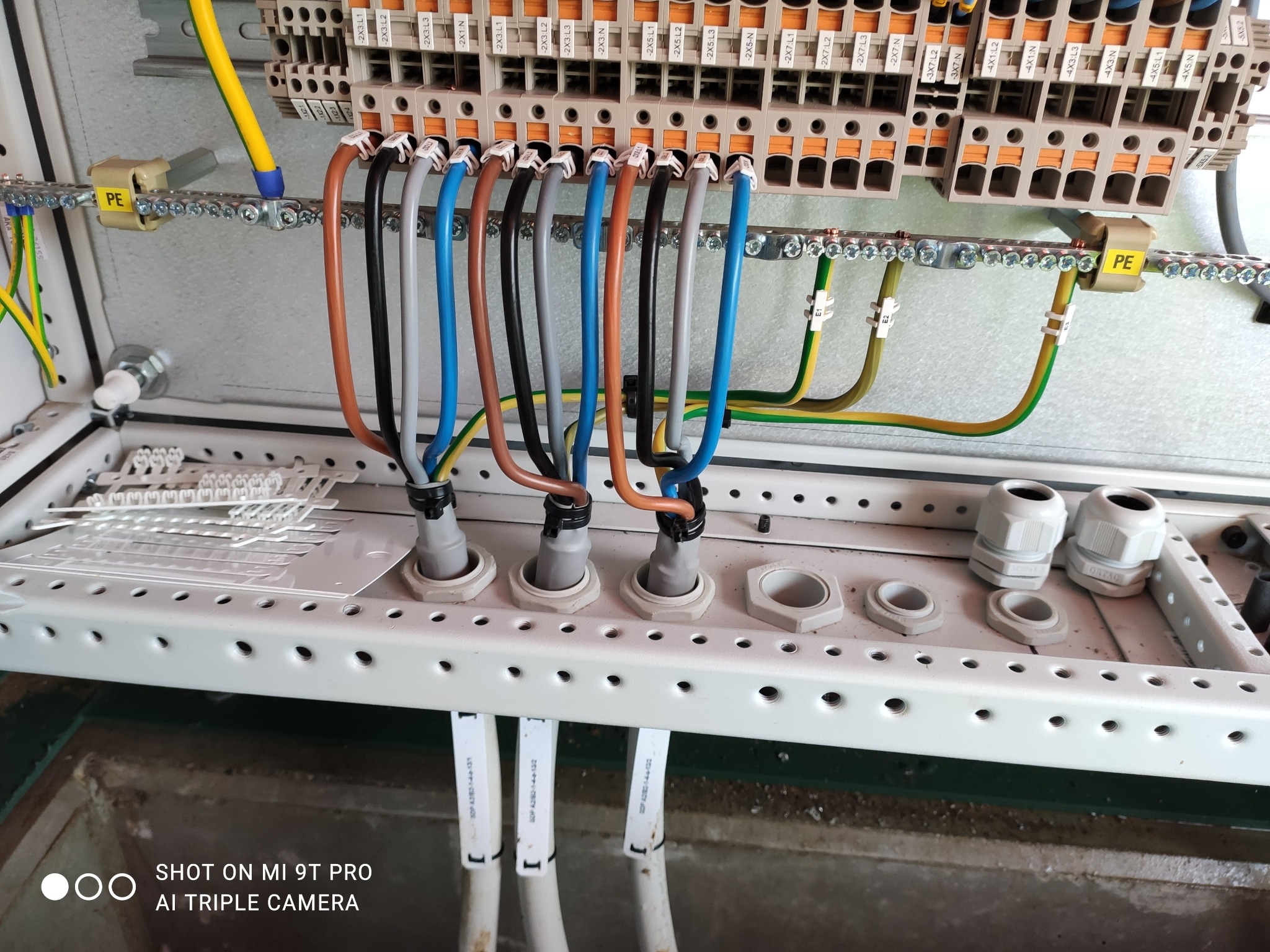 Szczegółowe ujęcie wnętrza skrzynki elektrycznej z podłączonymi przewodami o różnych kolorach, listwą zaciskową i elementami montażowymi. Widoczne kable i oznaczenia.