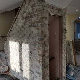 Leszek Zieleniewski - Wykończony fragment ściany z cegły dekoracyjnej nad drzwiami wewnątrz budynku. Widoczne narzędzia i zabezpieczenia podłogi. Nietypowe ułożenie cegły.