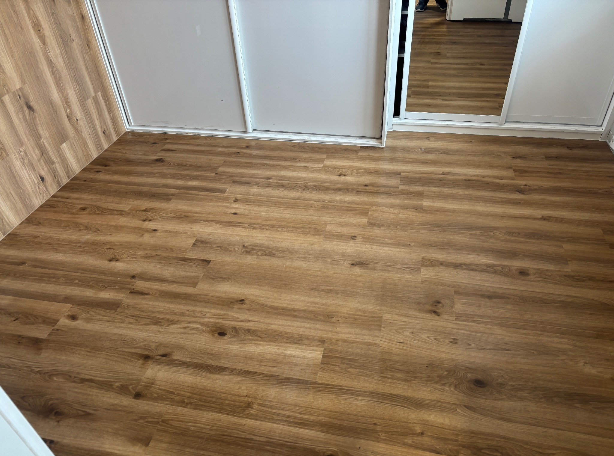 Ukończona podłoga z paneli w odcieniach brązu, ułożona w pokoju z białą szafą przesuwną. Widok z góry, panele z wyraźnym wzorem drewna.