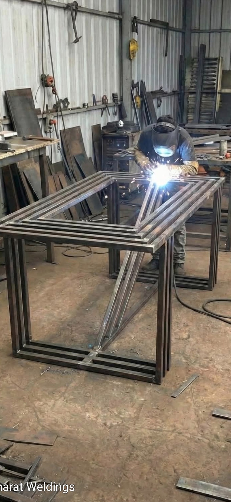 Spawacz w warsztacie łączy metalowe elementy konstrukcji stołu, iskry i jasne światło spawania, widoczne narzędzia i materiały.