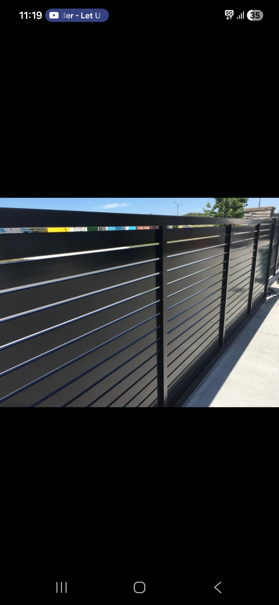 Nowoczesna, przesuwna brama wjazdowa z poziomymi panelami w kolorze antracytowym, widoczna z boku, z fragmentem chodnika i zieleni w tle.