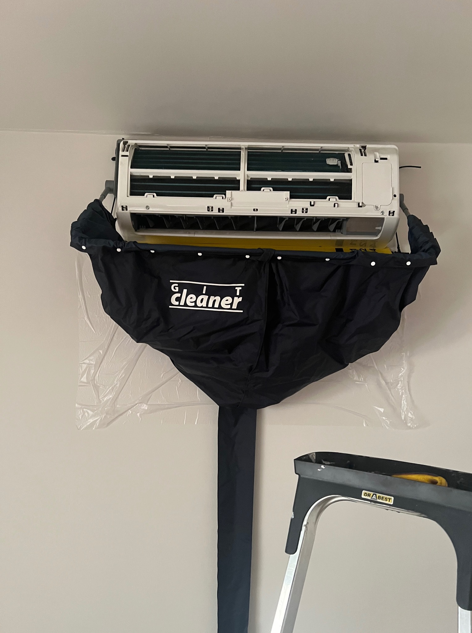 Czyszczenie klimatyzatora z użyciem specjalnego pokrowca 'GIT cleaner', drabina w tle. Widok z dołu na urządzenie podczas serwisu.