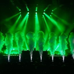 Nel Maczkiewicz - DJ na scenie podczas eventu, otoczony zielonymi światłami i dymem. Widoczny tłum publiczności. Dynamiczne ujęcie z koncertu.