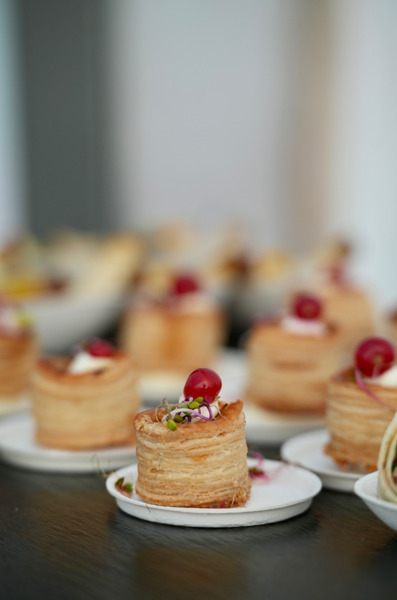 Elegancko podane, kruche babeczki z kremem i winogronem na białych talerzykach, tworzące apetyczny catering na imprezę. Delikatne oświetlenie podkreśla detale.