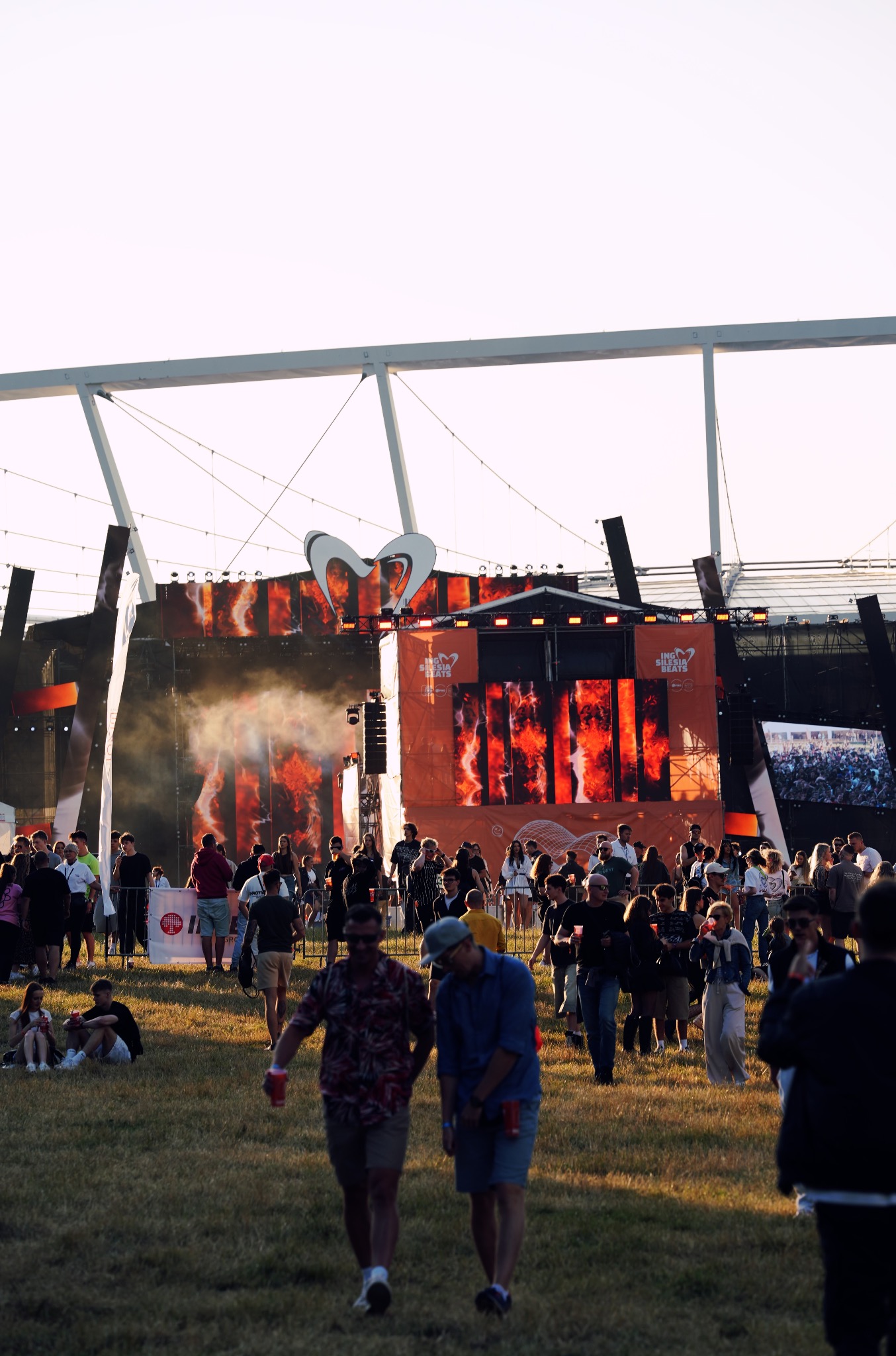 Widok na scenę z tłumem ludzi podczas festiwalu ING Silesia Beats, oświetloną pomarańczowym światłem, z widoczną konstrukcją dachu i logotypem imprezy.