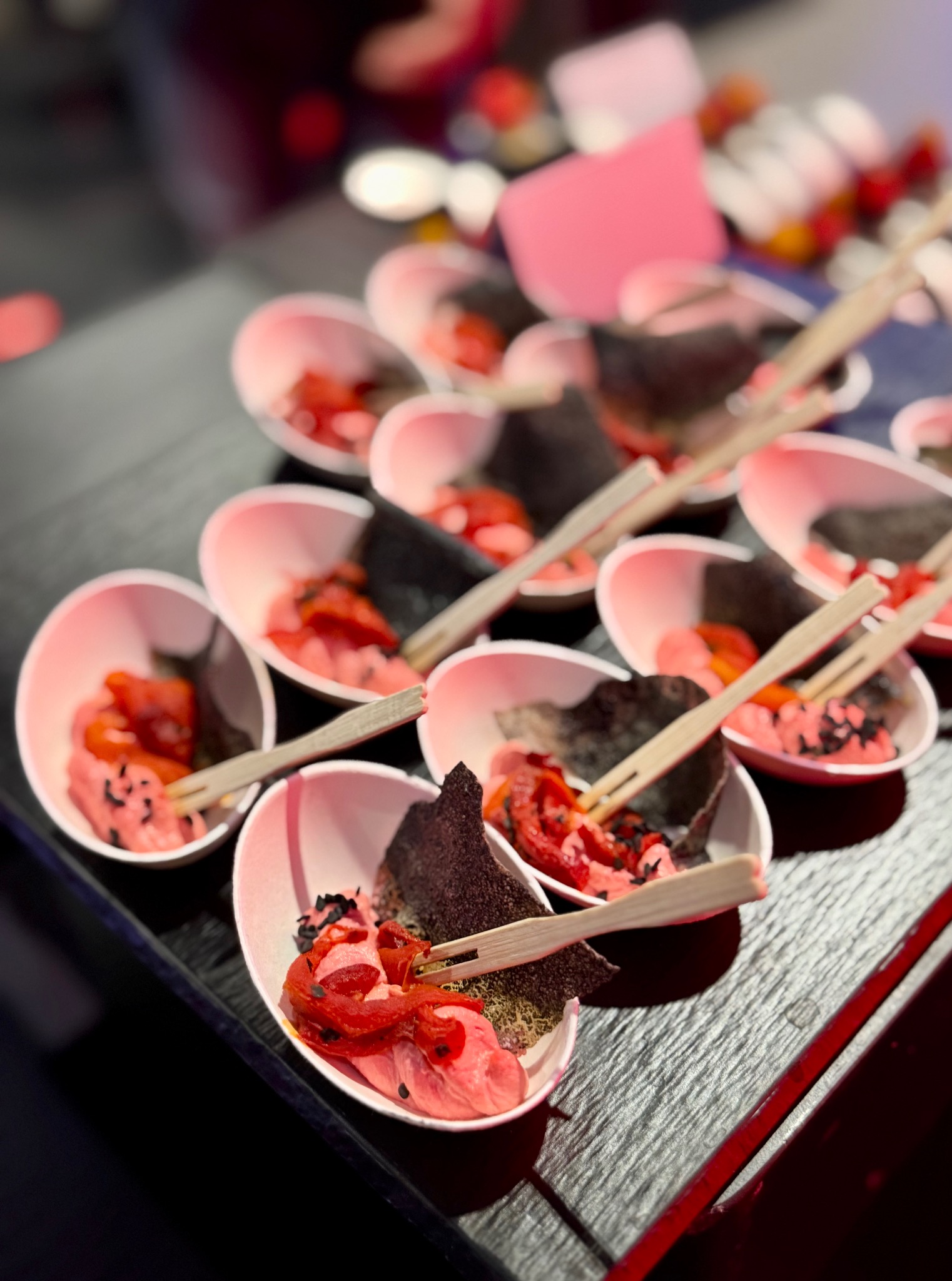 Ekskluzywny catering: porcje z czerwonymi warzywami, różowym musem i algami nori w białych miseczkach na czarnej tacy, podane z drewnianymi mini-widelcami.