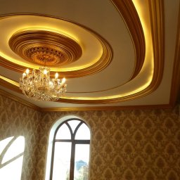 DEPOLDOM SPÓŁKA Z OGRANICZONĄ ODPOWIEDZIALNOŚCIĄ - Dekoracyjny sufit z oświetleniem LED i żyrandolem kryształowym, ściany z wzorzystą tapetą i łukowe okno, tworzące eleganckie wykończenie wnętrza.