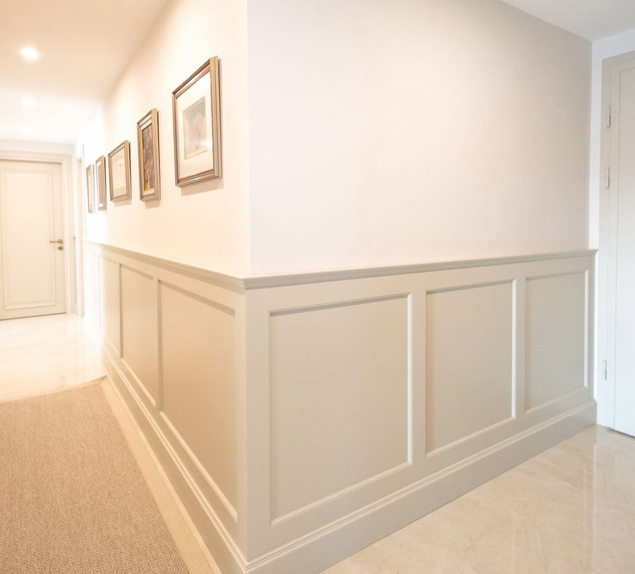 Korytarz z panelami ściennymi w stylu angielskim, kremowe ściany, marmurowa podłoga i obrazy w złotych ramach. Eleganckie wykończenie wnętrza.