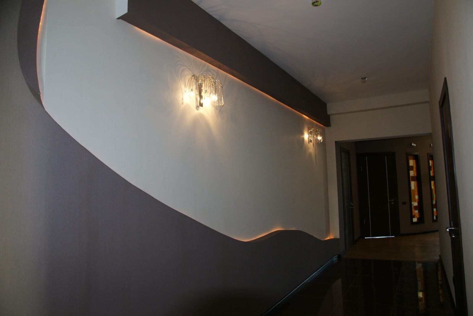 Nowoczesne wykończenie korytarza w Warszawie: dwukolorowa ściana z dekoracyjnym oświetleniem i designerskimi kinkietami. Elegancki minimalizm.