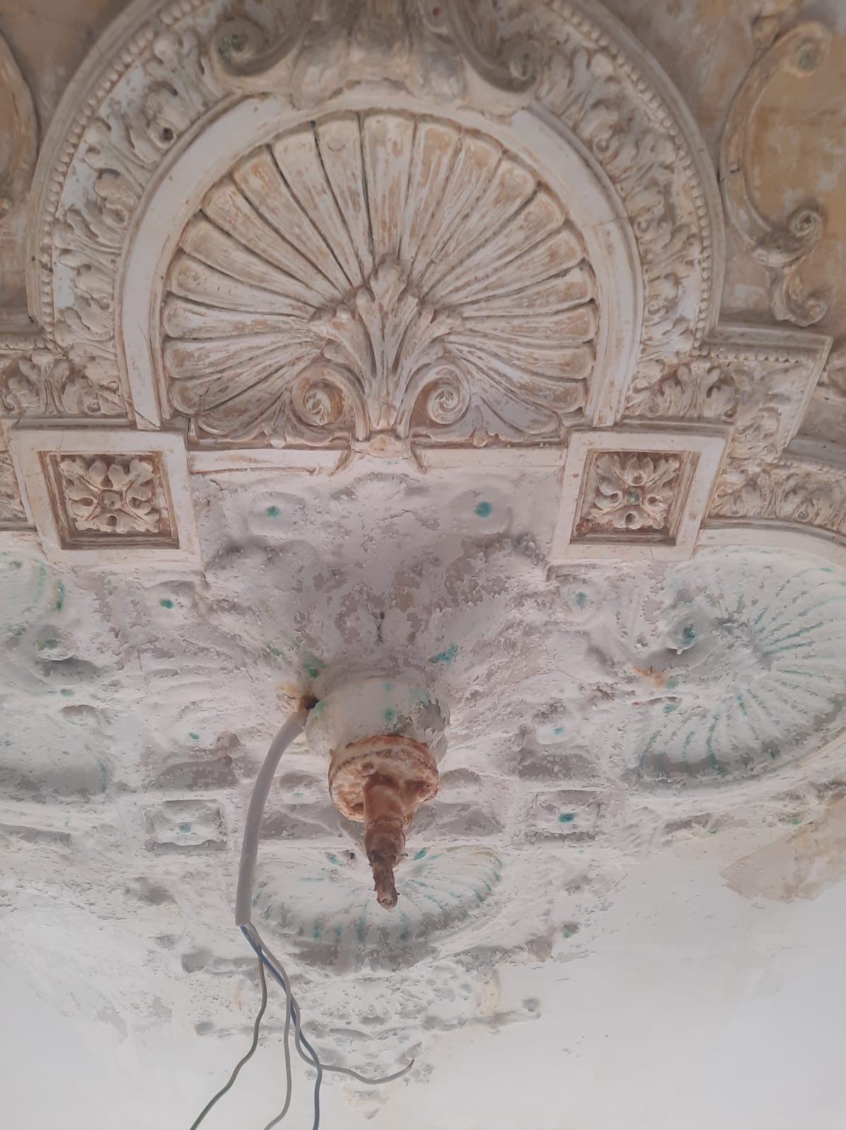 Dekoracyjny sufit z ornamentami i fragmentem instalacji elektrycznej, wymagający renowacji. Widoczne ślady użytkowania i potencjalne punkty do naprawy.