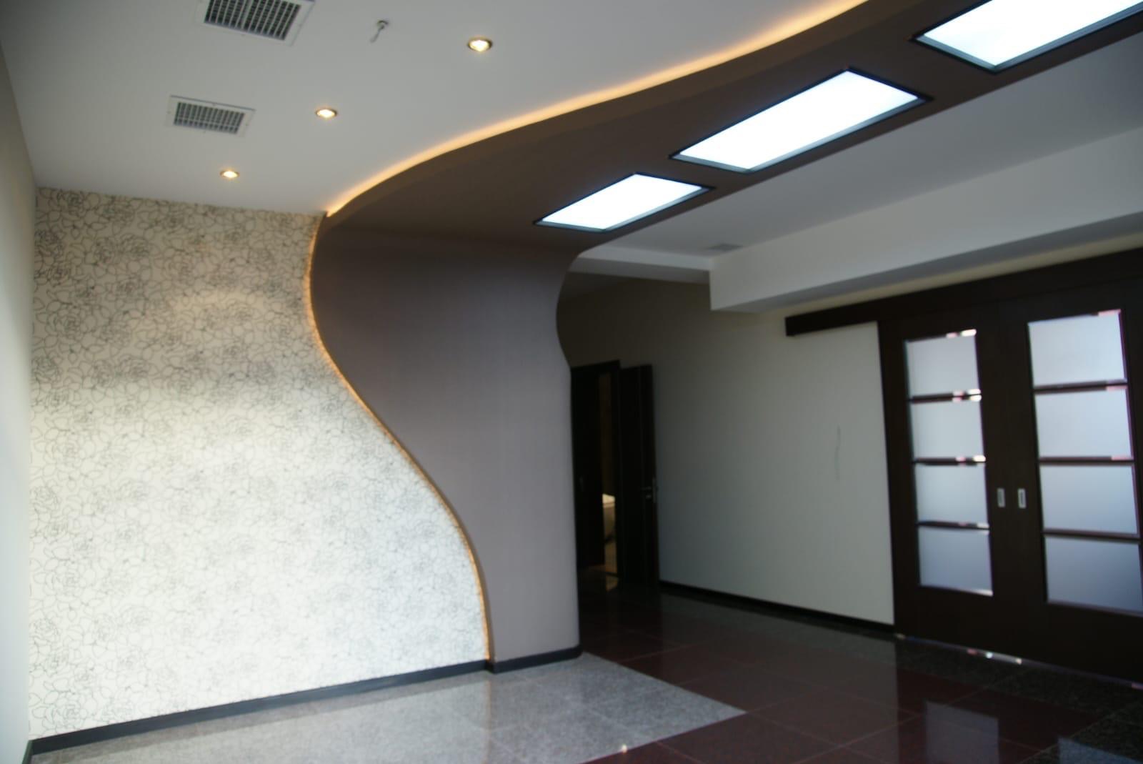 Nowoczesne wykończenie wnętrza z falistą ścianą z wzorem, podświetlonym sufitem i przesuwnymi drzwiami z matowego szkła. Eleganckie detale.