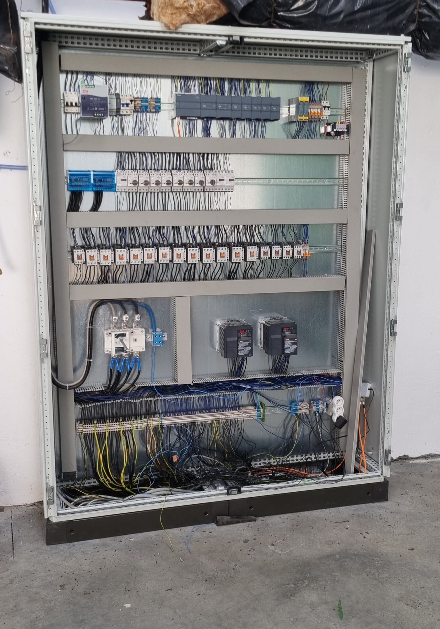 Rozdzielnica elektryczna z licznymi przewodami, bezpiecznikami i elementami sterującymi, widok z bliska na wnętrze szafy sterowniczej z metalową konstrukcją i uporządkowanymi kablami.