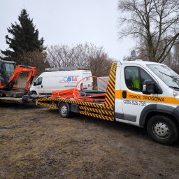 GRZEGORZ ZALESKI POMOC DROGOWA KWADRAT - Laweta z minikoparką Kubota i rurami na przyczepie, obok biały bus OrbitGaz Bytom. Pomoc drogowa, teren błotnisty, pochmurny dzień.