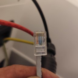 Krzysztof Burak - Szczegółowe zbliżenie wtyczki RJ45 z kolorowymi przewodami w dłoni, widoczne kable elektryczne w tle. Precyzyjne połączenie sieciowe.