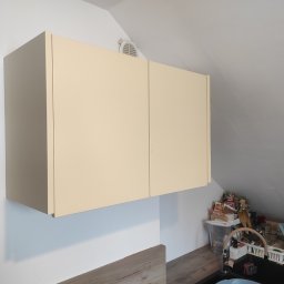 Tomasz Chmiel Hobbystycznie - Beżowa szafka kuchenna pod skosem dachu, z widocznym fragmentem blatu i zlewu. Minimalistyczny design, jasne wnętrze, wentylacja w suficie.