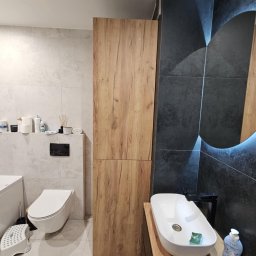 Tomasz Chmiel Hobbystycznie - Nowoczesna łazienka z drewnianą szafką i blatem pod umywalkę, czarne płytki z podświetlanym lustrem, biała ceramika. Minimalistyczny design.