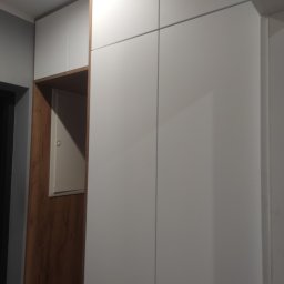 Tomasz Chmiel Hobbystycznie - Biała szafa wnękowa z drewnianym akcentem i ukrytym panelem elektrycznym, minimalistyczny design, oświetlenie sufitowe.