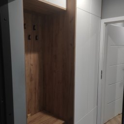 Tomasz Chmiel Hobbystycznie - Funkcjonalna szafa wnękowa z drewnianym wykończeniem i wieszakami, idealna do przedpokoju. Białe fronty szafy harmonizują z jasnym wnętrzem.