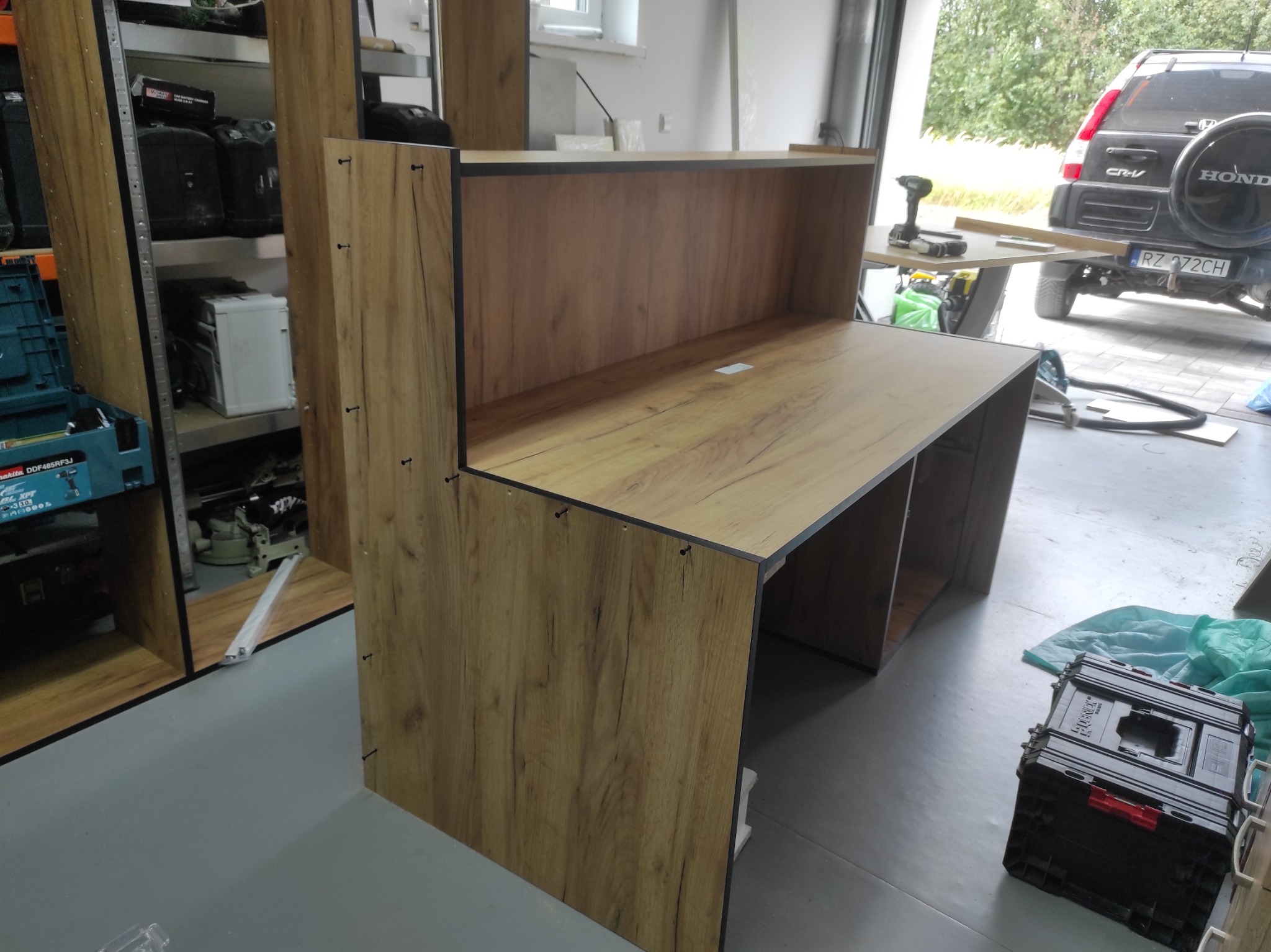 Montaż biurka z płyty drewnopodobnej w warsztacie; widoczne narzędzia i elementy szafki. Ujęcie z boku, ukazujące strukturę materiału i detale łączeń.