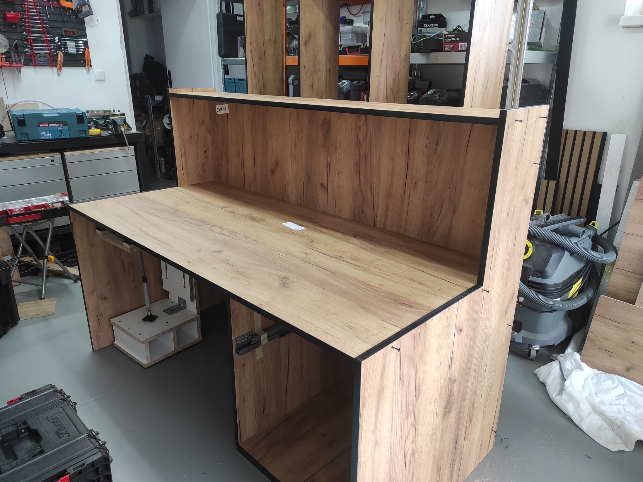 Stół roboczy z płyty drewnopodobnej w trakcie montażu, widoczne elementy mocujące i narzędzia w tle. Stolarnia.