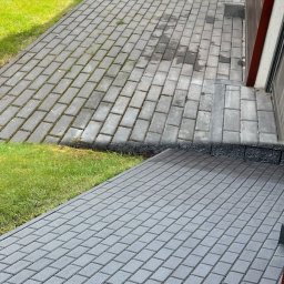 ServiceMaster.pl - Zdjęcie kostki brukowej przed i po czyszczeniu, widoczne różnice w kolorze i usunięty brud. Połowa powierzchni wyczyszczona, druga pokryta mchem i zabrudzeniami.