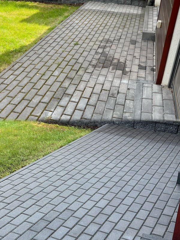 Zdjęcie kostki brukowej przed i po czyszczeniu, widoczne różnice w kolorze i usunięty brud. Połowa powierzchni wyczyszczona, druga pokryta mchem i zabrudzeniami.