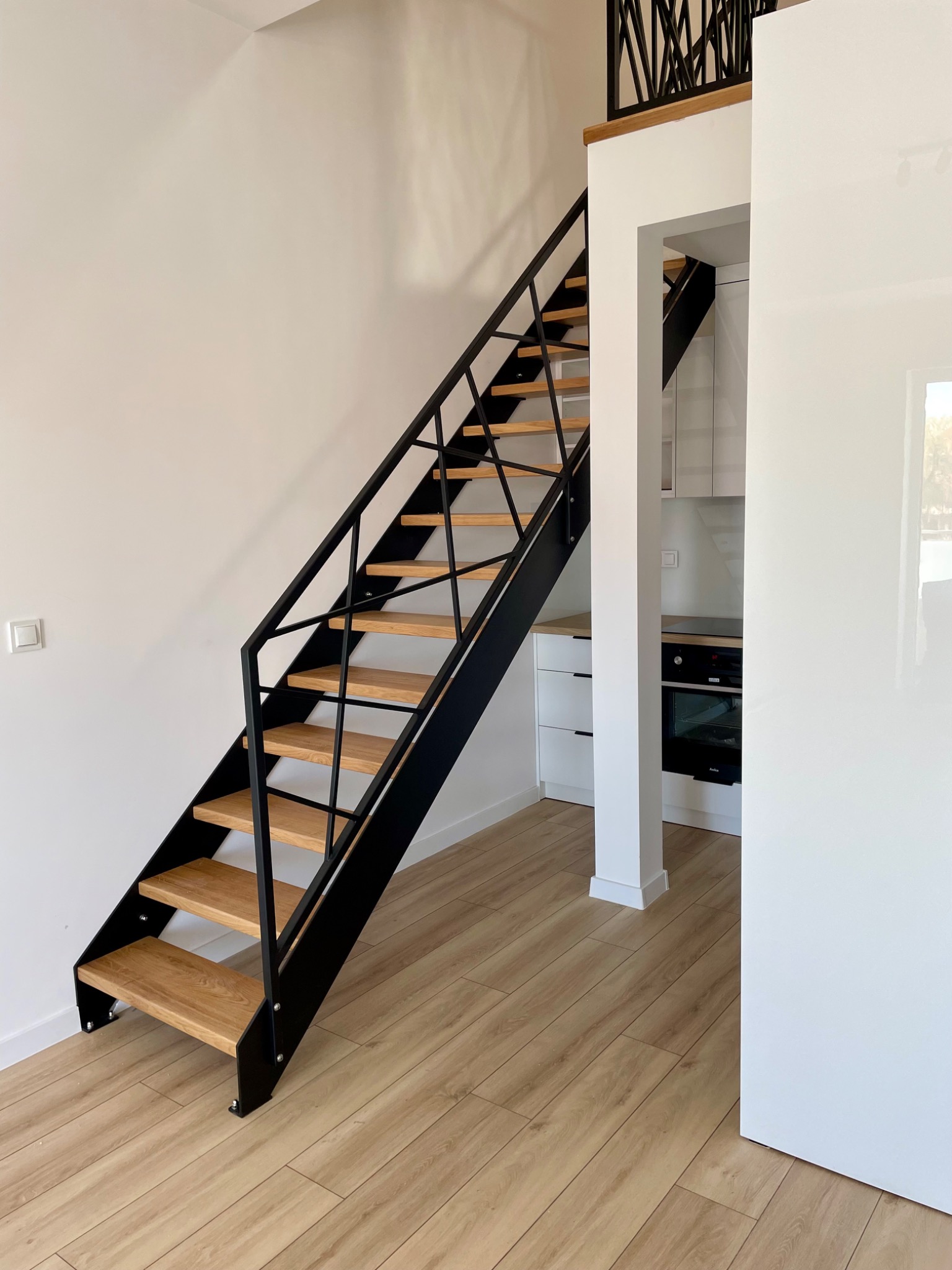 Nowoczesne schody metalowe z drewnianymi stopniami, czarna konstrukcja, jasne wnętrze, widok z dołu, minimalistyczny design, balustrada na antresoli.