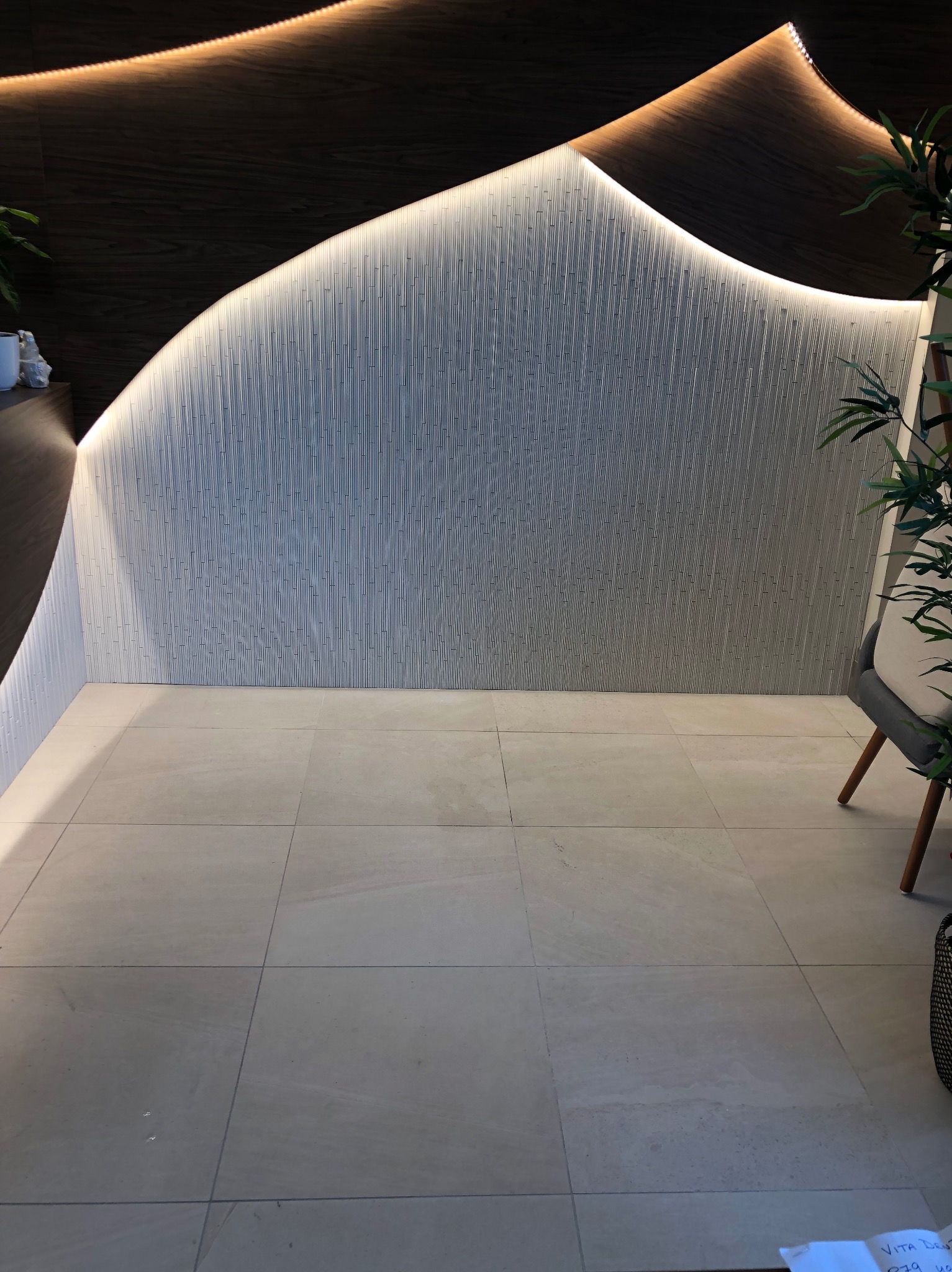 Nowoczesna łazienka z podświetlaną ścianą o fakturze pionowych pasków i jasnymi, kwadratowymi płytkami podłogowymi. Minimalistyczny design z elementami dekoracyjnymi.