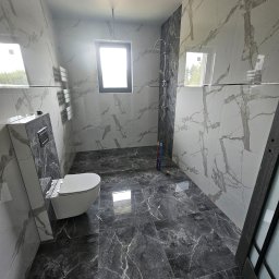 MBACZU MACIEJ CZUBA - Wykończona łazienka z marmurowymi płytkami na ścianach i podłodze, widoczna toaleta, grzejnik drabinkowy i kabina prysznicowa z deszczownicą. Nowoczesny design.