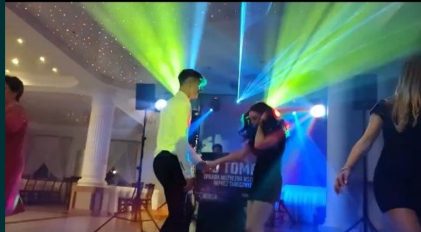 Para tańczy na parkiecie oświetlonym kolorowymi światłami, DJ za konsolą, sufit z efektem gwiazd. Impreza taneczna w lokalu.