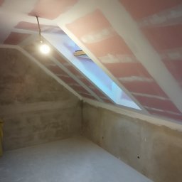 Wall Finish Łukasz Pacholski - Poddasze ze skośnym oknem dachowym w trakcie prac wykończeniowych. Widoczne płyty kartonowo-gipsowe na suficie i przygotowane ściany, oświetlone wiszącą żarówką.