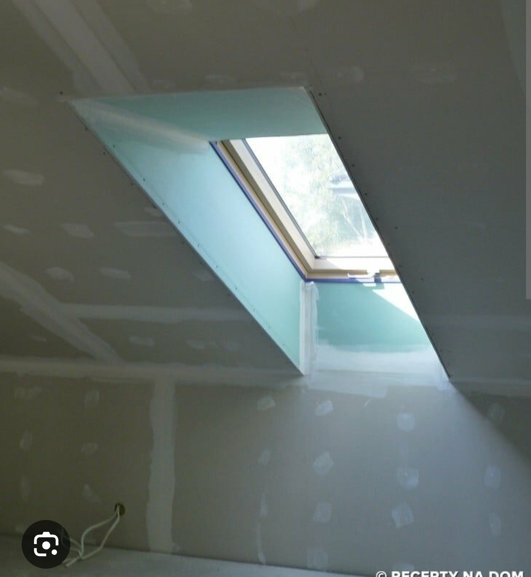 Montaż okna dachowego w skośnej ścianie z płyt kartonowo-gipsowych. Widoczne łączenia płyt i wystające przewody elektryczne w dolnej części.