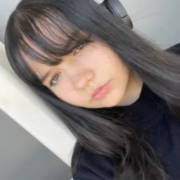 Portret kobiety z długimi, ciemnymi włosami i słuchawkami na głowie, opierającej się o białą balustradę, z delikatnym makijażem i naturalnym oświetleniem.