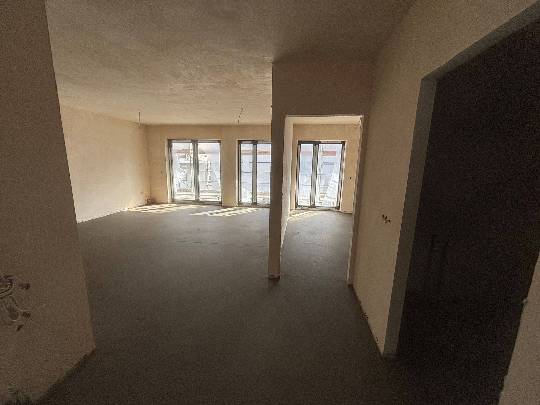 Wnętrze z wylaną, gładką posadzką jastrychową, widoczne okna balkonowe i surowy stan ścian. Dziennie światło podkreśla równość powierzchni.