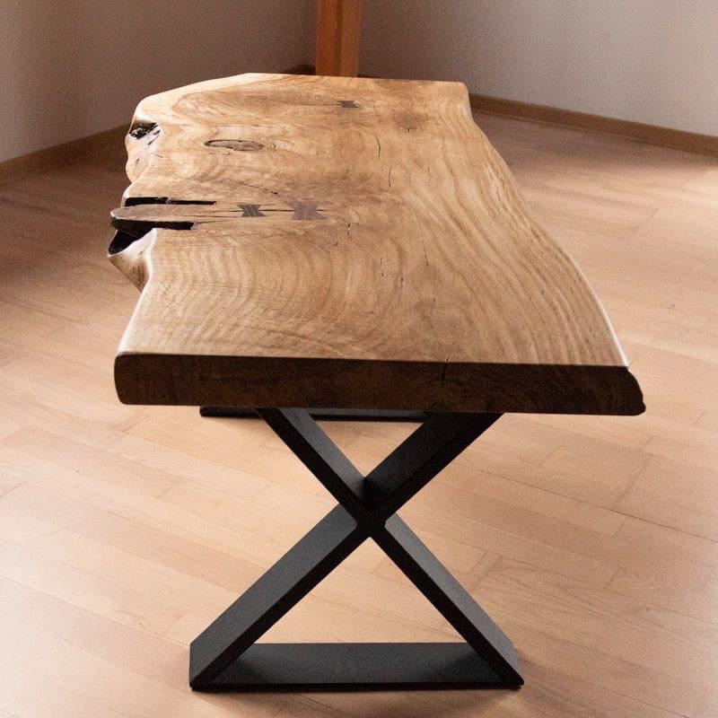 Stolik kawowy z blatem z litego drewna o nieregularnym kształcie i czarną, geometryczną podstawą. Widoczne słoje drewna i naturalne pęknięcia wypełnione żywicą.