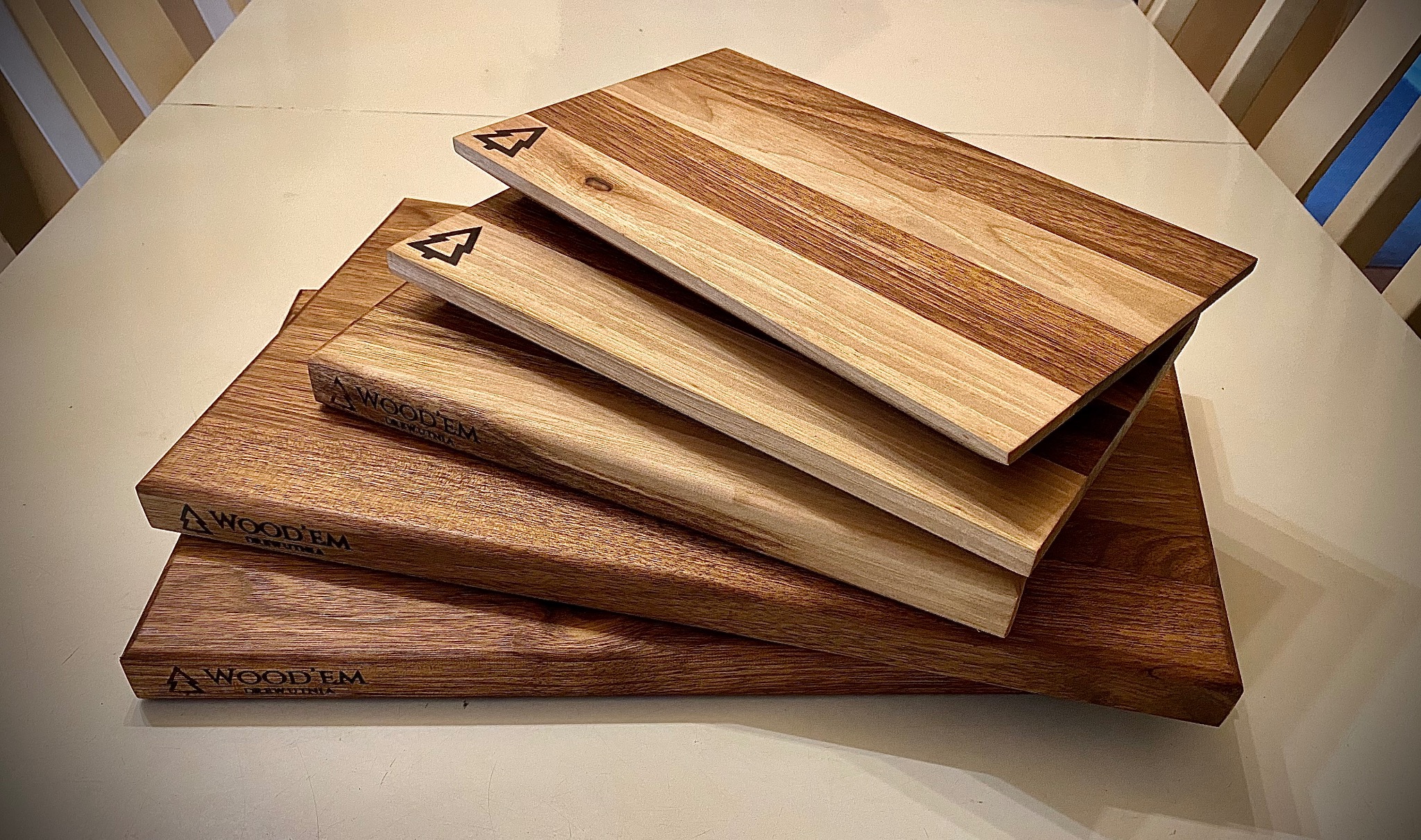 Stos desek z drewna o różnej kolorystyce ułożonych na blacie. Na deskach widoczne logo firmy z motywem drzewa. Deski o prostokątnym kształcie.