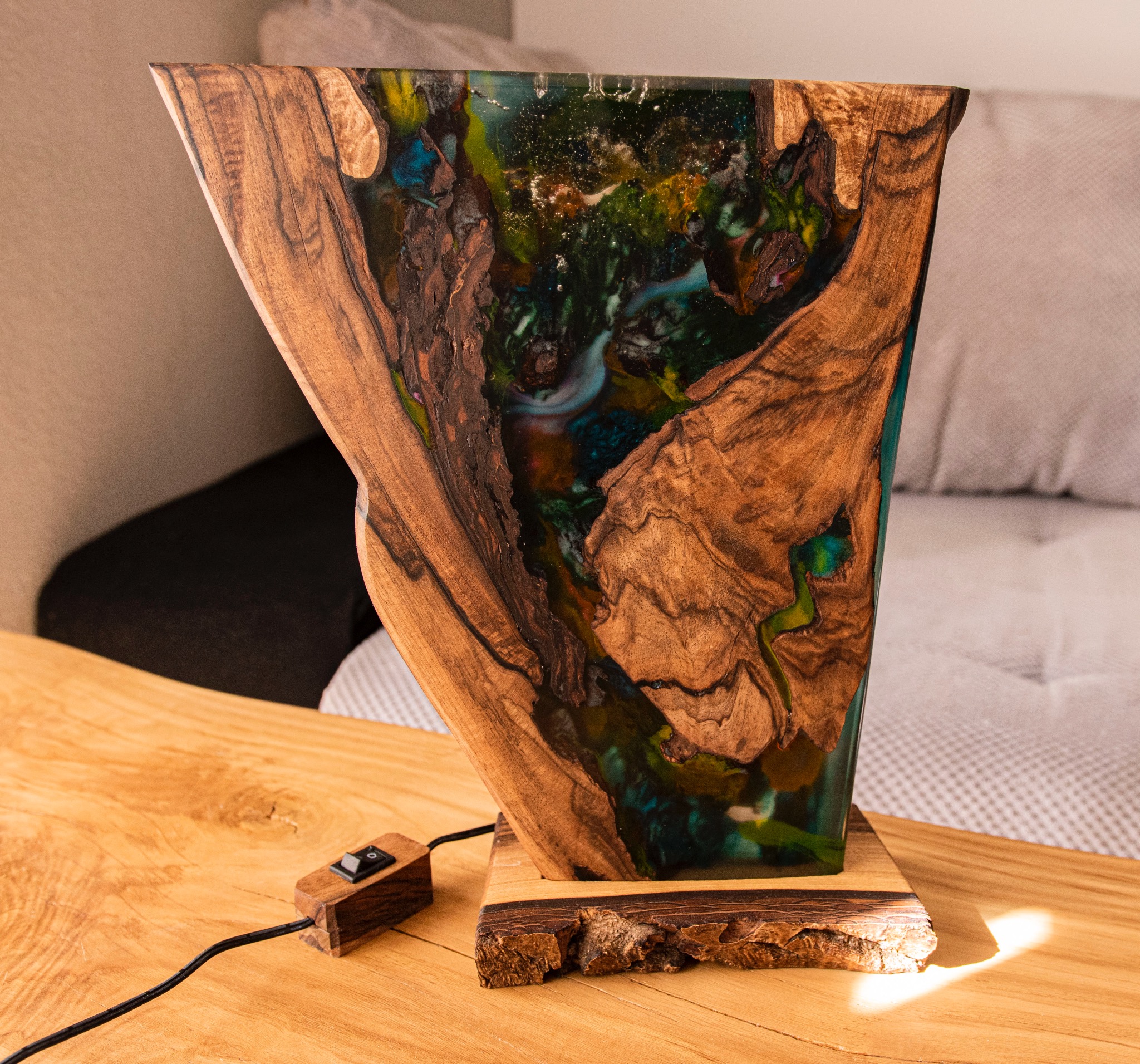 Unikatowa lampa z drewna orzechowego i żywicy epoksydowej, ukazująca przekrój z efektem głębi. Widoczny włącznik z drewna. Całość na blacie z widocznym usłojeniem.