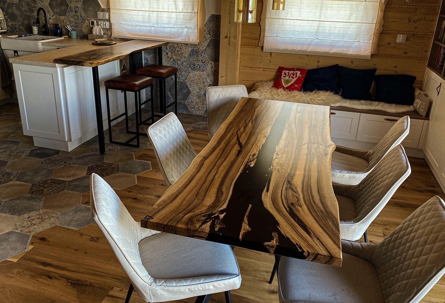 Stół z blatem z litego drewna z żywicą epoksydową w nowoczesnym wnętrzu z drewnianymi elementami, krzesłami i heksagonalną podłogą.