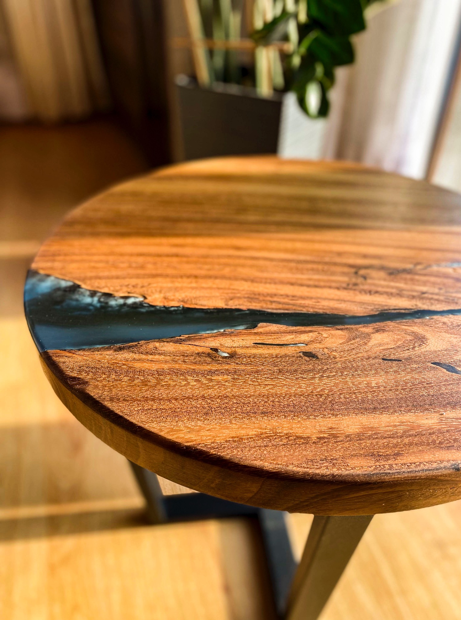 Okrągły stolik kawowy z drewna egzotycznego i żywicy epoksydowej na metalowej podstawie. Widoczne usłojenie drewna i detale wykończenia.