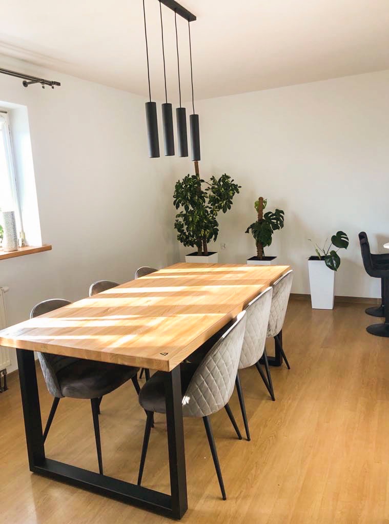 Drewniany stół z metalowymi nogami i krzesłami w jasnym wnętrzu w Szczawnicy. Nad stołem wisi lampa. Na podłodze panele, a w tle rośliny doniczkowe.