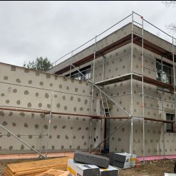 Yaroslav Dudych-Bondarenko D.B. Elewacja Expert - Dom w trakcie ocieplania: styropian XPS, warstwa kleju z kołkami, rusztowanie. Widoczne materiały budowlane.