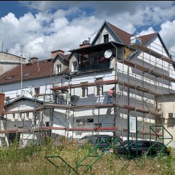 Yaroslav Dudych-Bondarenko D.B. Elewacja Expert - Ocieplanie budynku mieszkalnego w trakcie prac, widoczne rusztowania, pracownik i elementy ocieplenia. W tle błękitne niebo z chmurami.