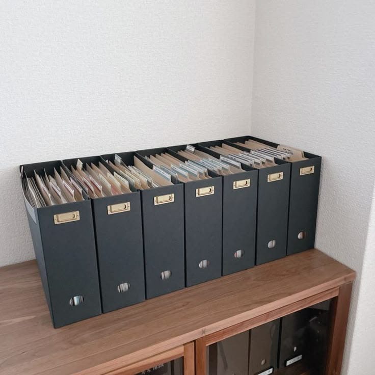 Rząd czarnych segregatorów z dokumentami na drewnianej szafce, uporządkowane archiwum biurowe w jasnym pomieszczeniu.