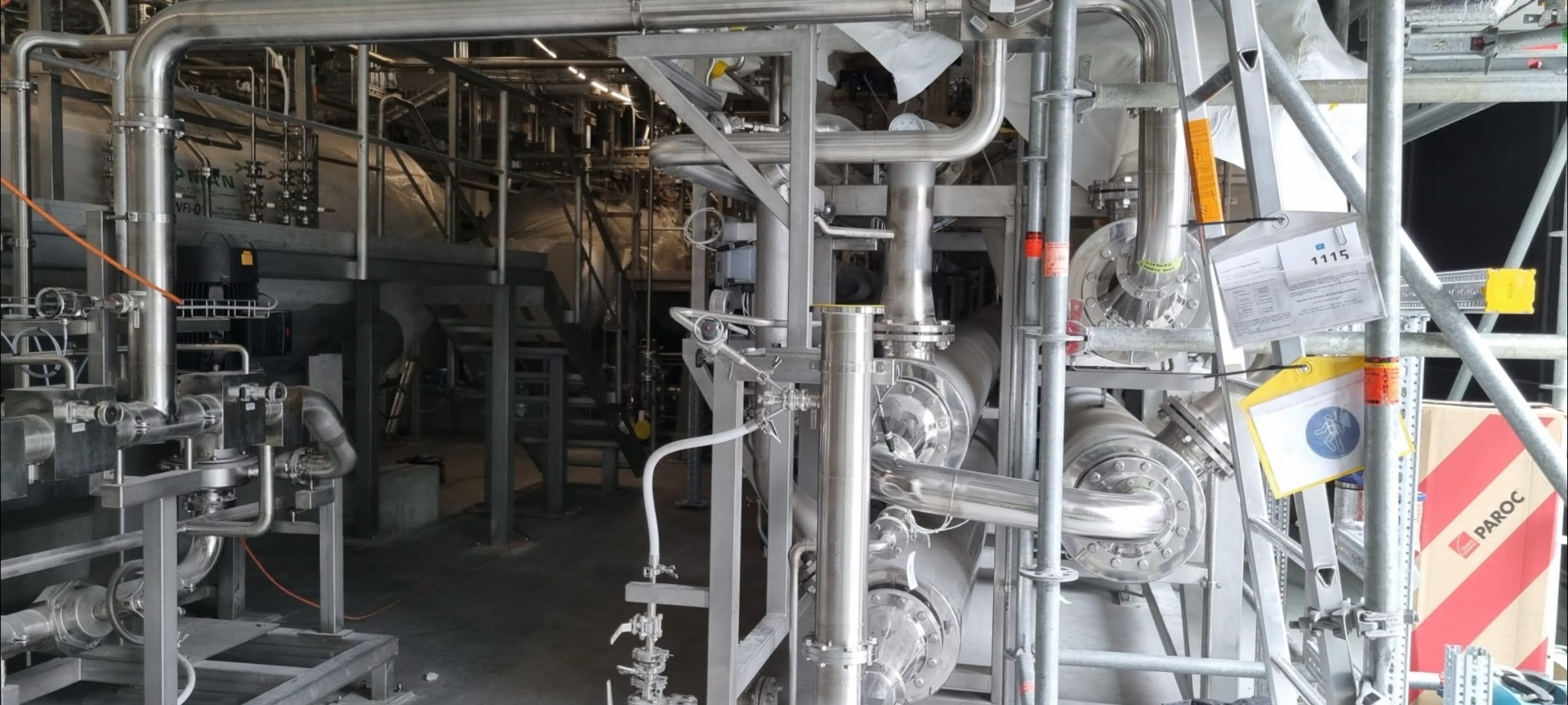 Kompleksowa instalacja przemysłowa z rur ze stali nierdzewnej, z widocznymi elementami rusztowania i dokumentacją techniczną na budowie.