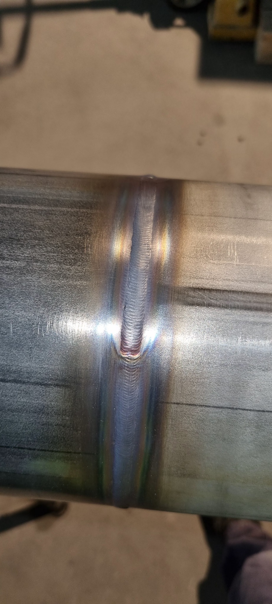 Spoina na metalowej rurze, widoczne tęczowe zabarwienie termiczne. Precyzyjne łączenie elementów, wysoka jakość wykonania. Detal spawalniczy.