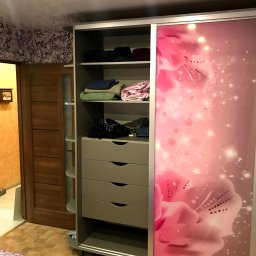 DENYS ZHABITENKO - Szafa wnękowa z przesuwnymi drzwiami, zdobiona motywem kwiatowym w odcieniach różu, z widocznymi półkami i szufladami, częściowo wypełniona ubraniami.