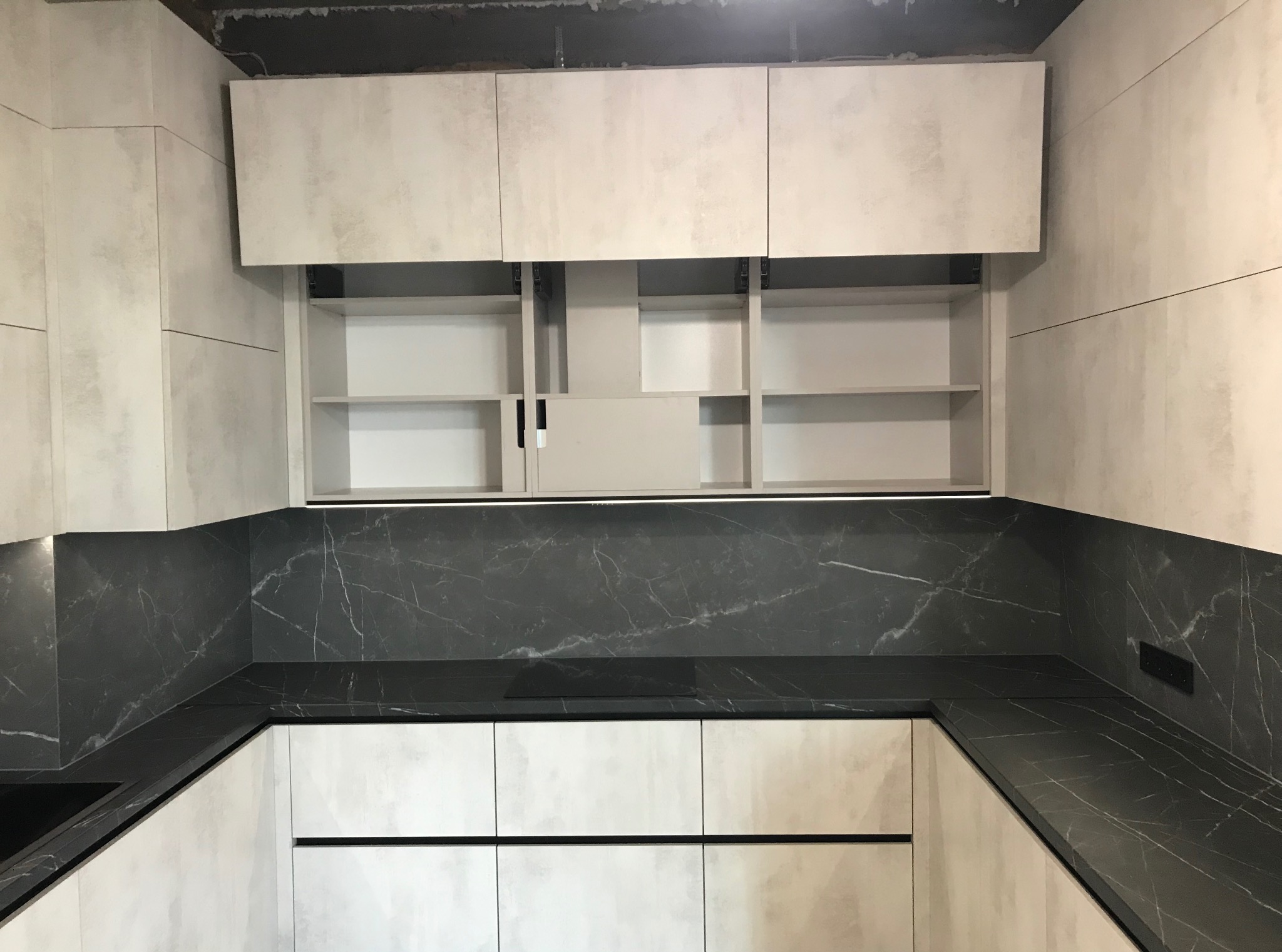 Jasna kuchnia z marmurowym blatem i otwartymi szafkami wiszącymi, ukazująca półki. Nowoczesny design z widocznymi detalami wykończenia.